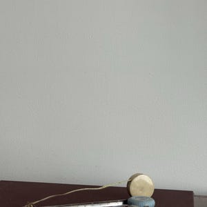 Może przedstawiać: Kolekcja zabytkowych narzędzi pomiarowych, w tym mosiężna miara taśmowa, metalowa linijka oraz małe czarno-czerwone k&oacute;łko pomiarowe. Przedmioty ułożone są na ciemnobrązowej powierzchni, sugerując motyw rzemiosła lub zabytkowych narzędzi.