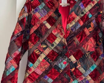 May include: A quilted jacket with a patchwork design. The jacket features a variety of fabrics in shades of red, burgundy, and other colors. The jacket has a collared neckline and button closures. The lining is red.