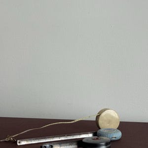 Może przedstawiać: Kolekcja zabytkowych narzędzi pomiarowych, w tym metalowa linijka, chowana miara taśmowa i dwie okrągłe miary taśmowe. Linijka pokazuje oznaczenia w centymetrach. Miary taśmowe są w kolorach beżowym, niebieskim i czarnym.