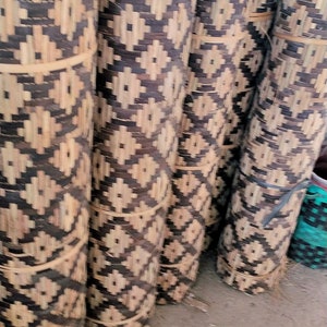 May include: Close-up of several rolled up mats made of woven natural materials. The mats have a geometric pattern of brown and beige.