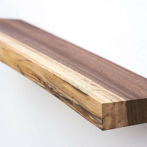 May include: A long, wooden shelf with a natural edge and a dark brown finish. The shelf is made of solid wood and has a rustic look.