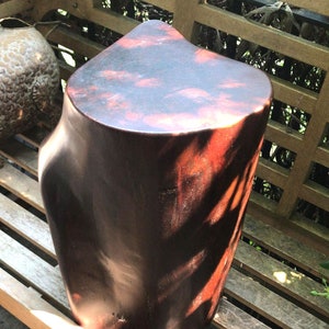 May include: A dark brown wooden stool with a smooth, rounded top. The stool has a natural wood grain pattern and a slightly irregular shape.