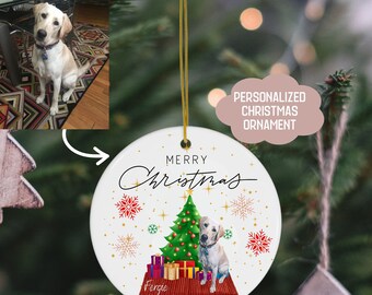 May include: White ceramic Christmas bauble featuring a green Christmas tree, red and gold presents, and a yellow dog sitting in front of the tree. The bauble has the text "Merry Christmas" in black cursive writing, the name "Fergie" in black cursive writing, and the year "2023" in black text.