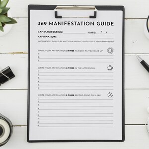 May include: A black clipboard with a white sheet of paper titled "369 Manifestation Guide". The paper has a section for writing an affirmation and instructions to write it 3 times in the morning, 6 times in the afternoon, and 9 times before bed.