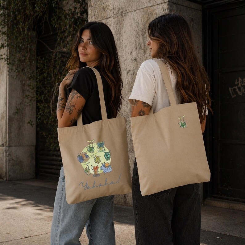 May include: Two beige tote bags. One bag features a colorful cartoon design with the word "Yahaha!" in a light blue script. The other bag has a small green and blue design. Both bags have long handles.