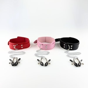 May include: Three leather collars in red, pink, and black, each with a silver chain and a pair of black nipple clamps. The collars have a buckle closure and are displayed against a white background.