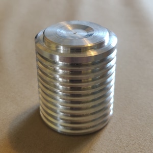 May include: A silver metal cylinder with a smooth top and a series of ridges along the sides.