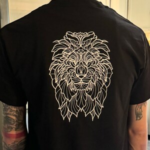 Könnte beinhalten: Schwarzes T-Shirt mit einem weißen Umriss eines Löwenkopfes. Das Löwenkopf besteht aus komplizierten Mustern.