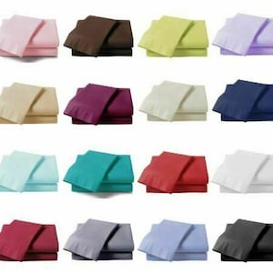 May include: A selection of folded bed sheet sets in a variety of colours, including pink, brown, yellow, purple, beige, burgundy, white, navy blue, light blue, teal, red, grey, and black. Each set includes a top sheet and a fitted sheet.