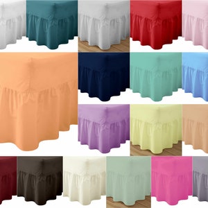 May include: A selection of bed skirts in a variety of solid colours, including white, teal, red, pink, orange, navy, mint, and blue. Each skirt has a ruffled edge, adding a decorative element to bedding. The skirts are arranged in a grid.