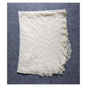 May include: A rectangular piece of off-white lace fabric featuring a delicate floral pattern throughout. The fabric has a scalloped edge along one side, showcasing intricate openwork details and a soft, semi-sheer texture across the entire surface.