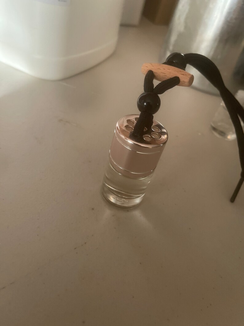 May include: A clear glass bottle with a silver cap and a black string with a wooden bead. The bottle has small holes in the cap and is hanging from the string.