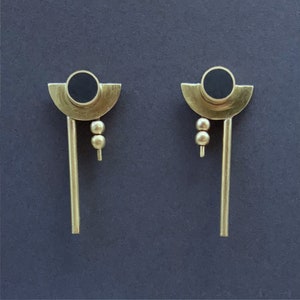May include: A pair of gold earrings with black circles and small gold beads hanging from the bottom.