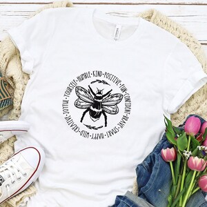 May include: White t-shirt with a black and white bee graphic and the text "FUN-CONFIDENT-BRAVE SMART-HAPPY-WILD-CREATIVE-JOYFUL-YOURSELF-HUMBLE-KIND-POSITIVE".