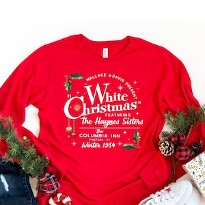 May include: Red long-sleeve shirt with a white graphic print that reads "Wallace & Davis Present "White Christmas" Featuring The Haynes Sisters The Columbia Inn Pinetree VT Winter 1954".