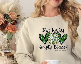May include: A beige sweatshirt with the text "Not lucky Simply Blessed Romans 4:7-8" and a green shamrock with gold glitter inside a heart.