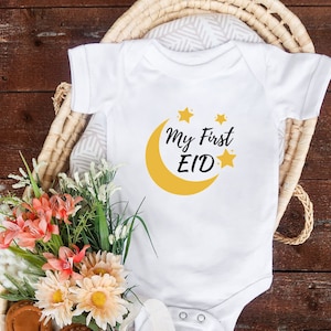 K&ouml;nnte beinhalten: Wei&szlig;er Baby-Strampler mit einem gelben Halbmond- und Sternen-Design. Der Text "My First Eid" ist auf dem Strampler aufgedruckt.