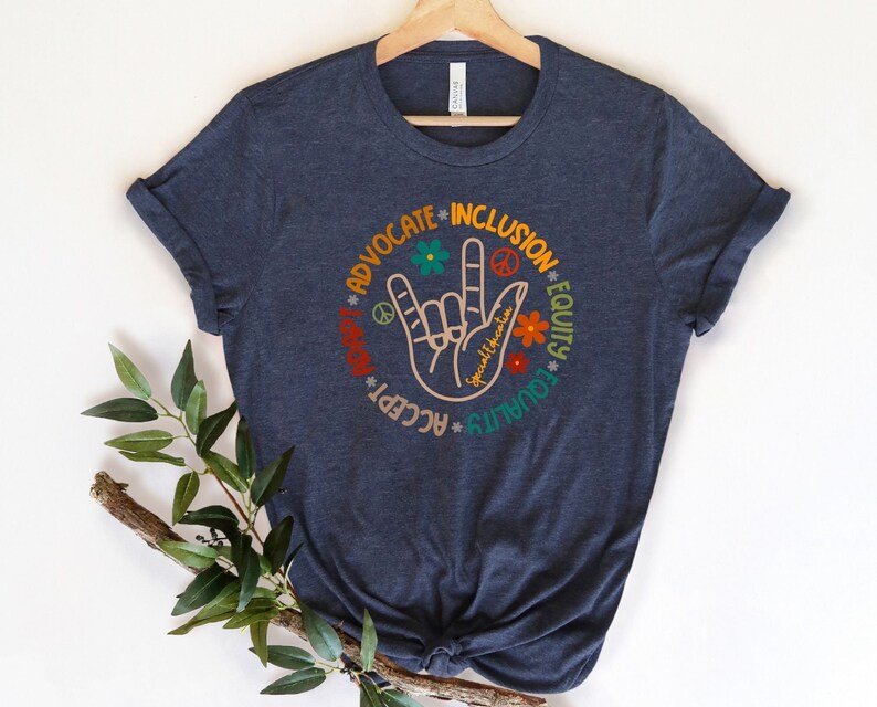 May include: A navy blue t-shirt with a graphic of a hand making the American Sign Language sign for "I love you". The graphic is surrounded by the words "Advocate", "Inclusion", "Equity", "Equality", "Love", "Accept", and "Peace" in a circle.