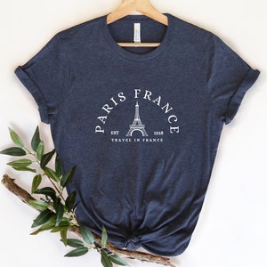 May include: A navy blue t-shirt with a white graphic of the Eiffel Tower and the text "Paris France Est 1928 Travel in France".