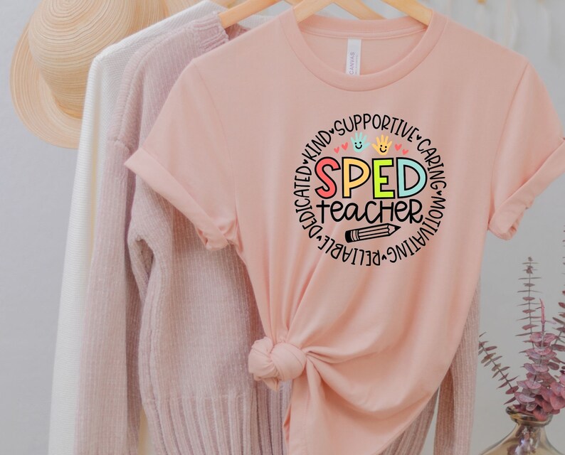Pode incluir: Uma camiseta rosa com um design circular que diz "SPED teacher" em letras coloridas. O c&iacute;rculo &eacute; cercado por palavras como "dedicado", "amig&aacute;vel", "solid&aacute;rio", "carinhoso", "motivador", "confi&aacute;vel" e "destac&aacute;vel".