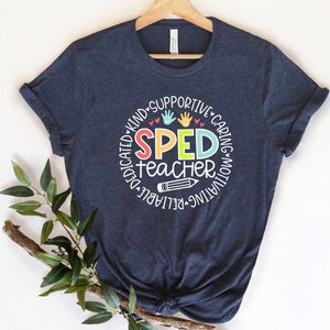 Pode incluir: Uma camiseta azul marinho com um design circular branco que diz "SPED teacher" em letras coloridas. O c&iacute;rculo &eacute; rodeado pelas palavras "dedicado, gentil, solid&aacute;rio, atencioso, motivador, confi&aacute;vel" em branco.