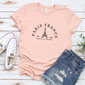 May include: A light pink t-shirt with a black graphic of the Eiffel Tower and the text "Paris France Est 1928 Travel in France".