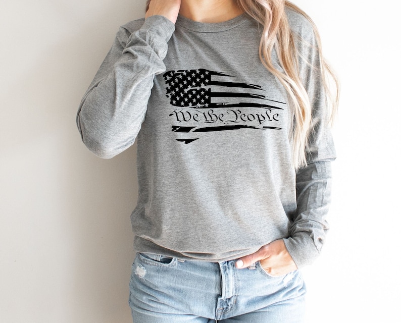 May include: A gray long-sleeved shirt with a distressed American flag design and the text "We the People" printed in black.