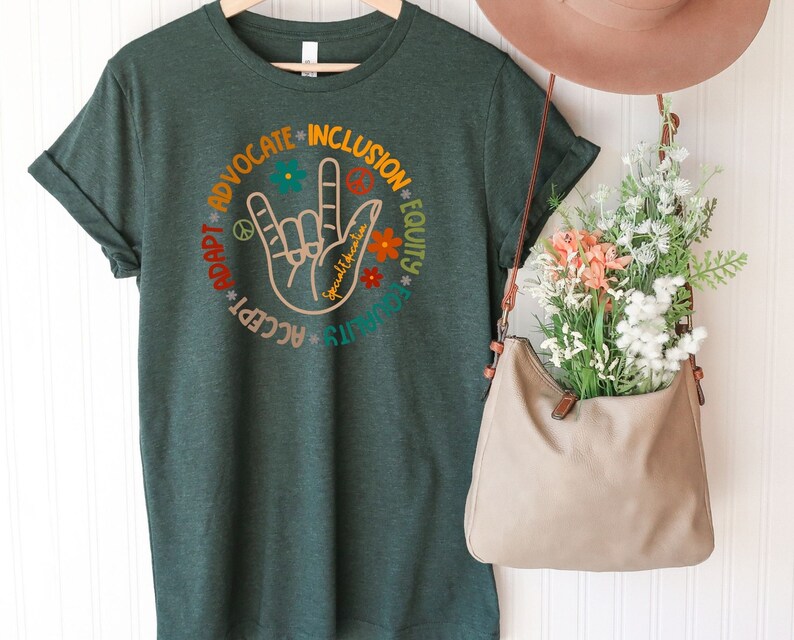 May include: A dark green t-shirt with a circular design featuring the American Sign Language symbol for "I love you" surrounded by the words "Advocate", "Inclusion", "Equity", "Accept", "Adapt", "Listen", and "Spread kindness".