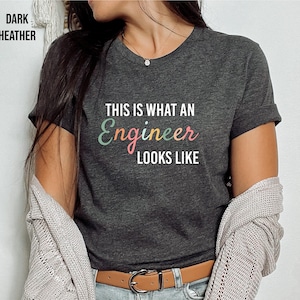 Puede incluir: Una camiseta gris oscuro jaspeada con el texto "This is what an Engineer looks like" en letras de colores.