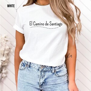 a woman wearing a white t - shirt with the words el camino de santiago