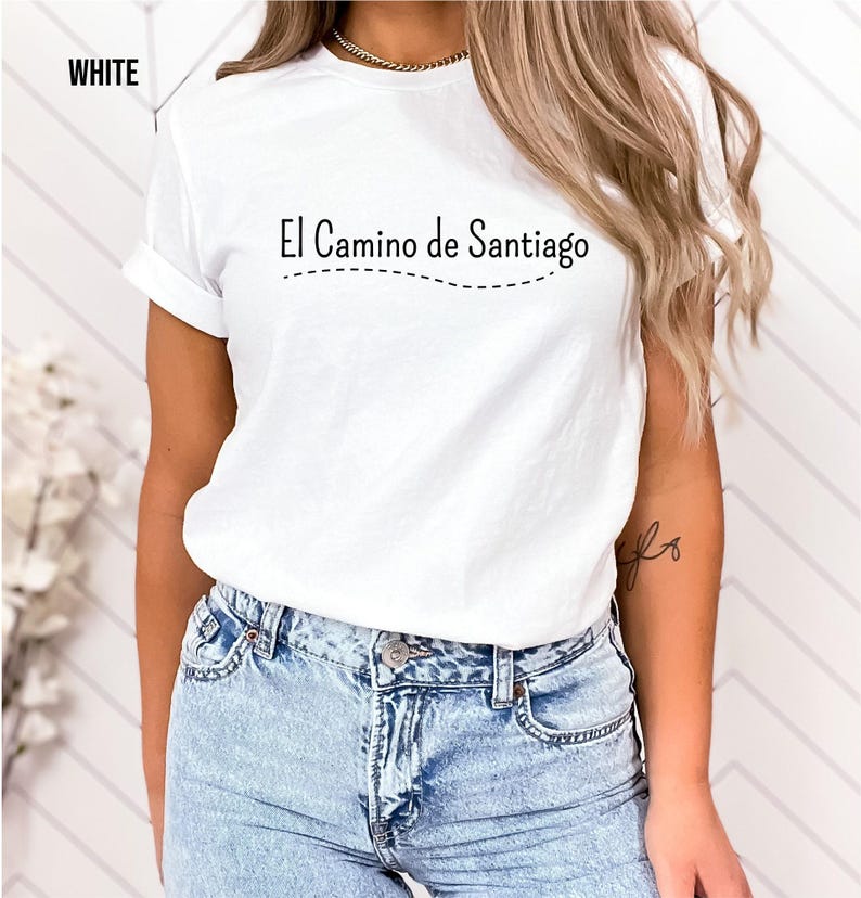 a woman wearing a white t - shirt with the words el camino de santiago