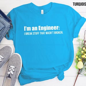 Op de afbeelding: Turquoiseblauw T-shirt met witte tekst die luidt: "Ik ben een ingenieur: Ik breek dingen die niet kapot waren."