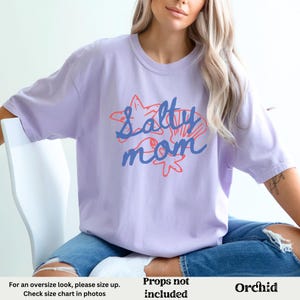 May include: A lavender t-shirt with the text "Salty Mom" in blue and red lettering. The text is surrounded by a graphic of seashells and starfish.