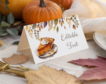 May include: A white folded place card featuring a watercolour illustration of a slice of pumpkin pie with whipped cream on a plate, decorated with autumn leaves at the top, and the black text Editable Text printed on the right side.