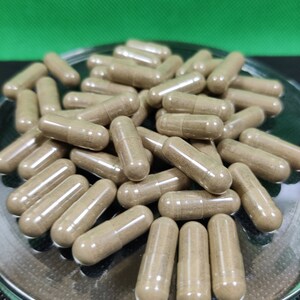 May include: A close-up image of a pile of brown capsules in a clear glass dish. The capsules are translucent and show the brown powder inside.