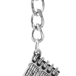 May include: Silver keychain with a silver chain and a charm that looks like a notebook with musical notes and the text "Symphony No. 5".