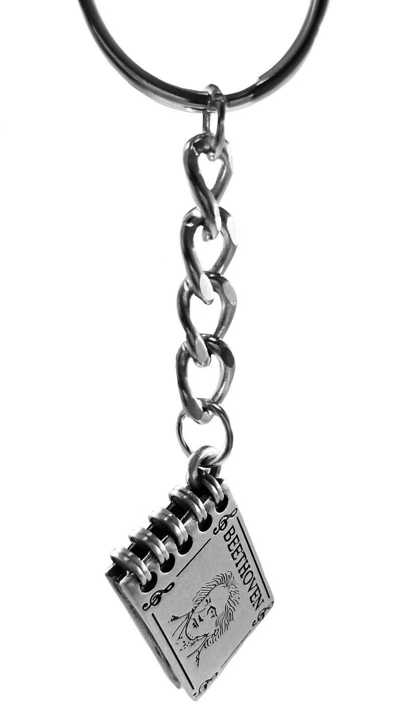 May include: Silver keychain featuring a small notebook charm with a portrait of Beethoven and the text "BEETHOVEN".