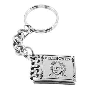 May include: Silver keychain featuring a small book-shaped charm with a portrait of Beethoven and the text "BEETHOVEN" surrounded by musical notes.