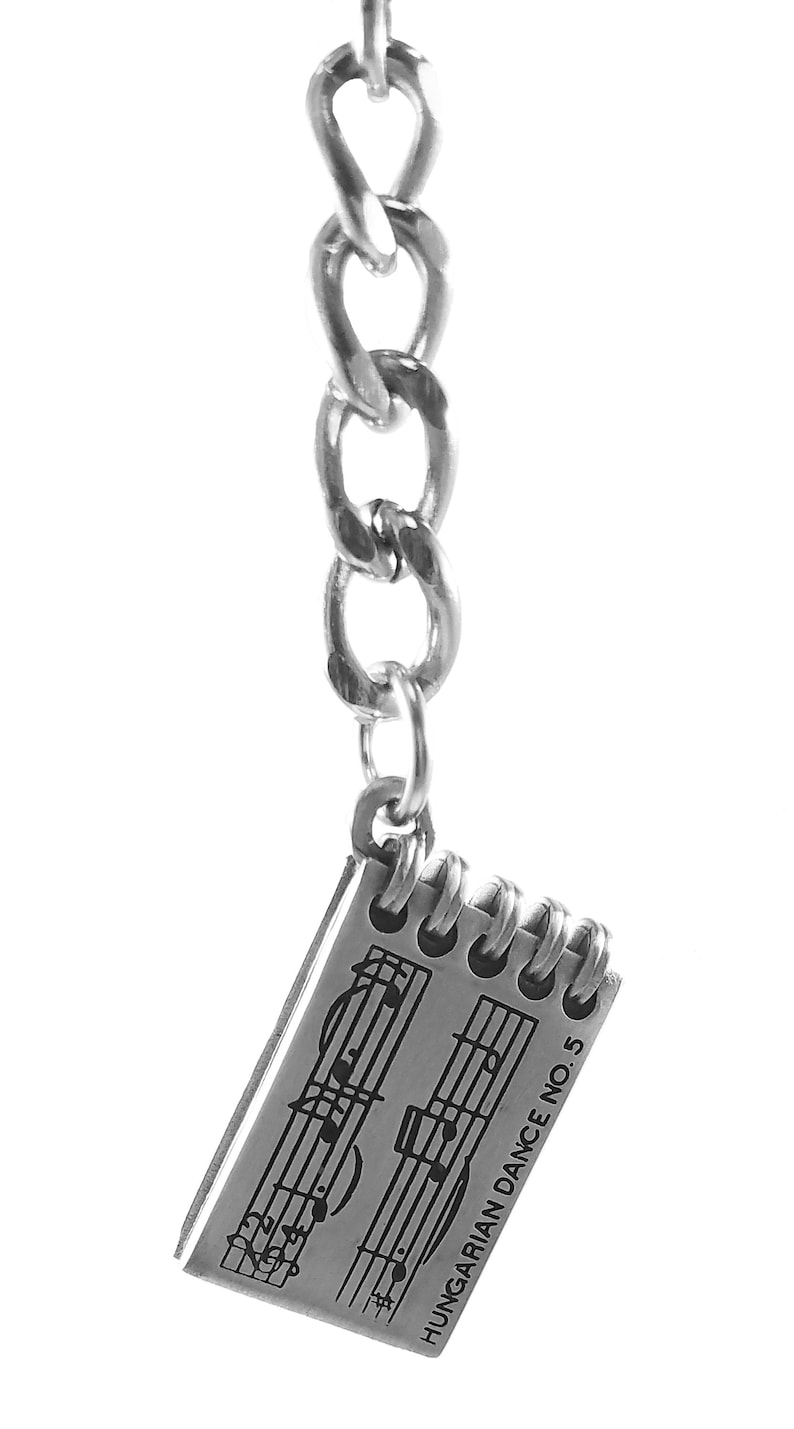 May include: A silver charm keychain featuring a small notebook with musical notes and the text "HUNGARIAN DANCE NO. 5".