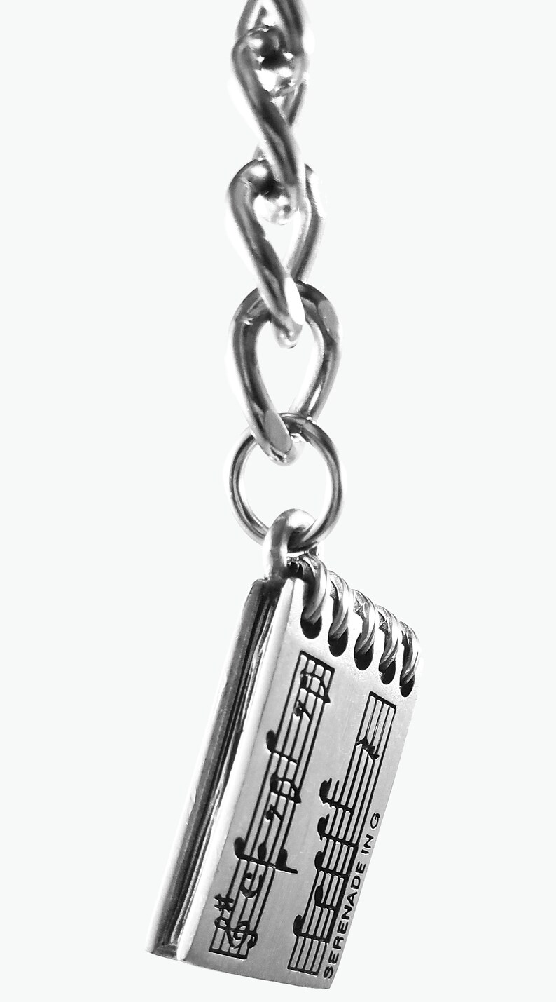 May include: Silver charm keychain featuring a small notebook with musical notes and the text "SERENADE IN G".