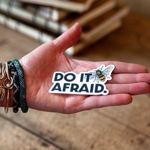 May include: A white sticker with the text "DO IT AFRAID." in blue lettering. A cartoon bee with black and yellow stripes is flying above the text.