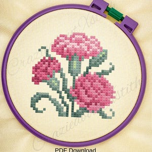 May include: Cross-stitch embroidery of pink flowers with green stems and leaves, set within a purple embroidery hoop. The design features three large flowers and the text "PDF Download" at the bottom. The background is a light beige fabric.