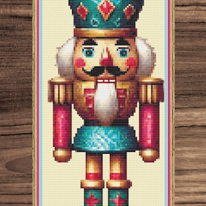 Pode incluir: Uma figura de quebra-nozes de estilo vintage com um uniforme azul e dourado, um chapéu vermelho e dourado e uma barba branca. O quebra-nozes está em pé sobre uma base dourada.