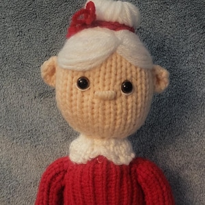 Puede incluir: Muñeca de punto hecha a mano de la Sra. Claus. La muñeca tiene una cara color melocotón, cabello blanco y un atuendo rojo y blanco. La muñeca lleva un delantal blanco y zapatos negros. Una decoración festiva.