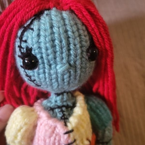 May include: A knitted doll with red yarn hair, blue yarn skin, and a multi-colored patchwork dress. The doll has black yarn eyes and a stitched mouth.