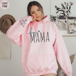 a woman wearing a pink hoodie with the word mama on it