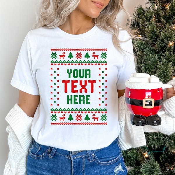 May include: A white short-sleeved t-shirt featuring a red and green holiday-themed pattern with the text YOUR TEXT HERE in the center. The design includes small reindeer and pine tree motifs arranged in a rectangular border on the front.