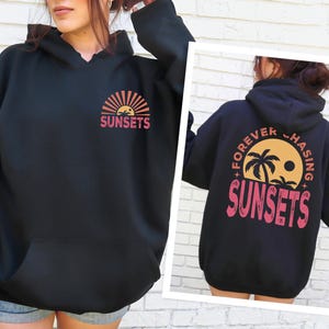 a woman wearing a black sweatshirt with sunsets on it