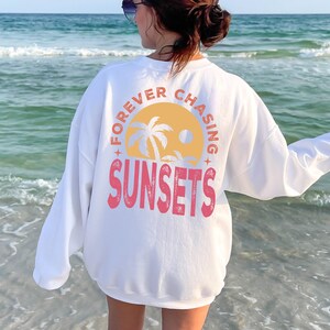 a woman standing on the beach wearing a white sweatshirt