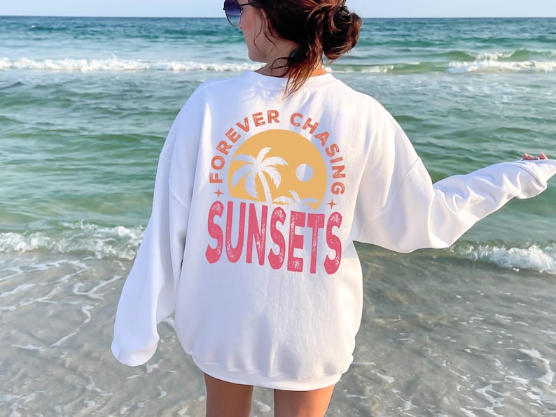 a woman standing on the beach wearing a white sweatshirt